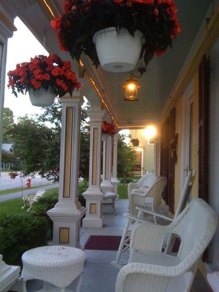 Side view of the covered front porch with white wicker chairs and hanging baskets with red flowers