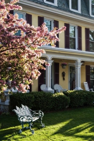The Inn's exterior with yellow siding, covered front porch and flowering tree