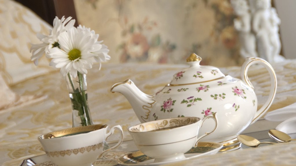 Guest bed with silver platter topped with beautiful ivory and gold teapot, cups and saucers