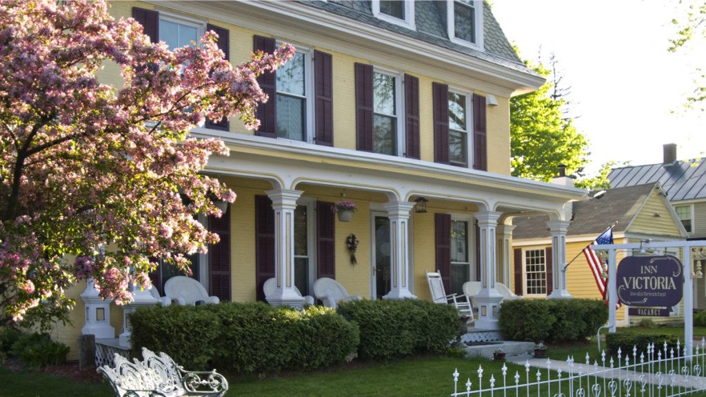 The Inn's exterior with yellow siding, covered front porch and flowering tree