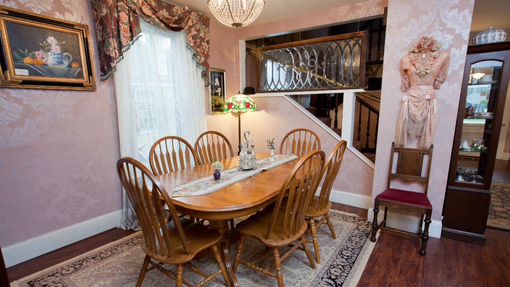 Guest dining room with oval table, six chairs, in front of a window with white sheer curtains