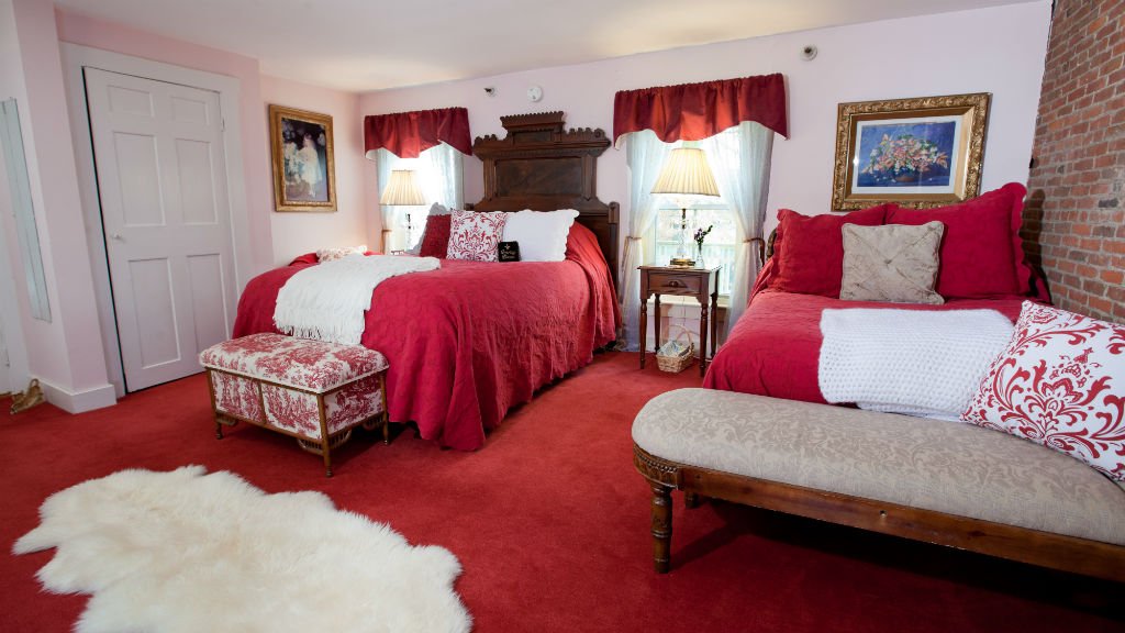 Guest room with red carpet and bedding, two windows, and two benches at the foot of the beds