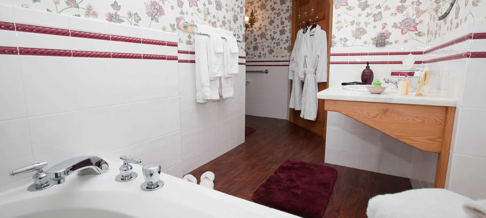 Prince Albert guest bath with white walls and floral wallpaper, tub and sink with hanging white robes