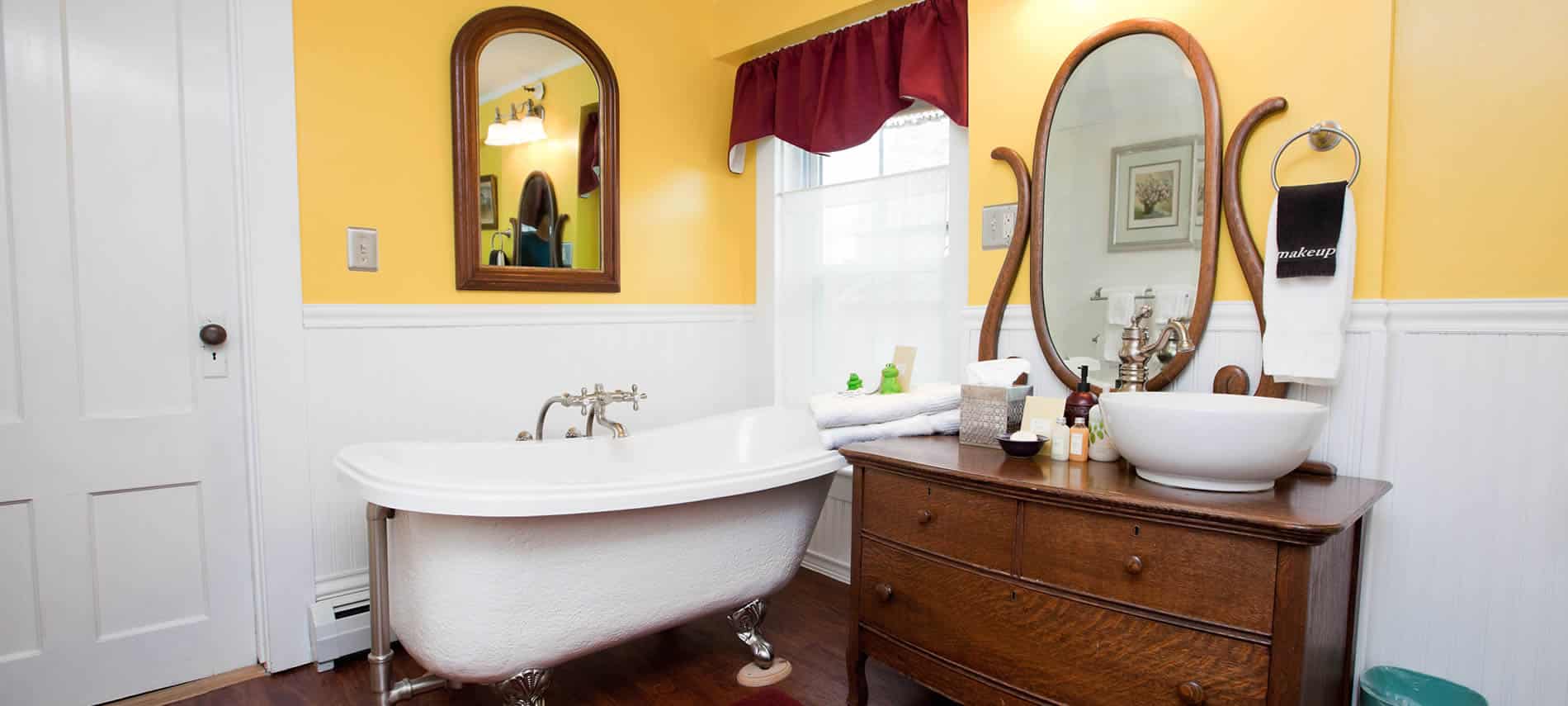 Prince Alfred guest bath with white and yellow walls, clawfoot tub and antique vanity with vessel sink and mirror