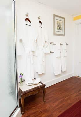 Prince Alfred guest bath with corner shower, wood floor, hanging white robes and white towels