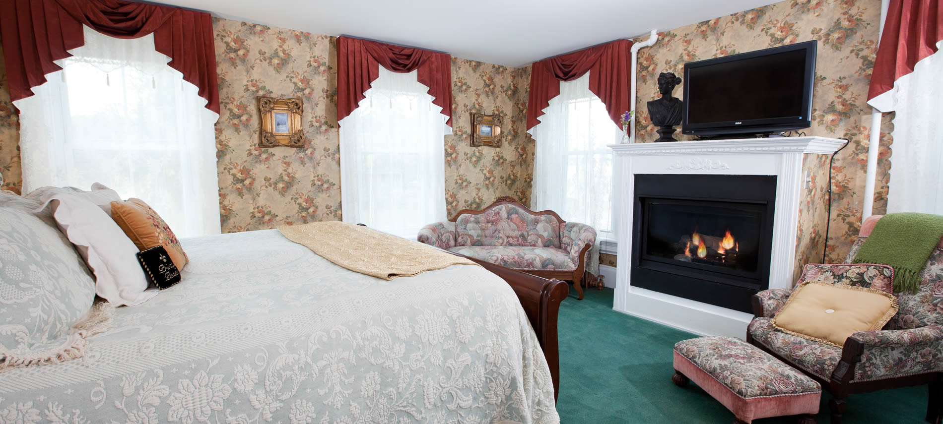 Princess Alice guest room, floral wallpaper, teal green carpet, fireplace, TV, upholstered furniture and several windows
