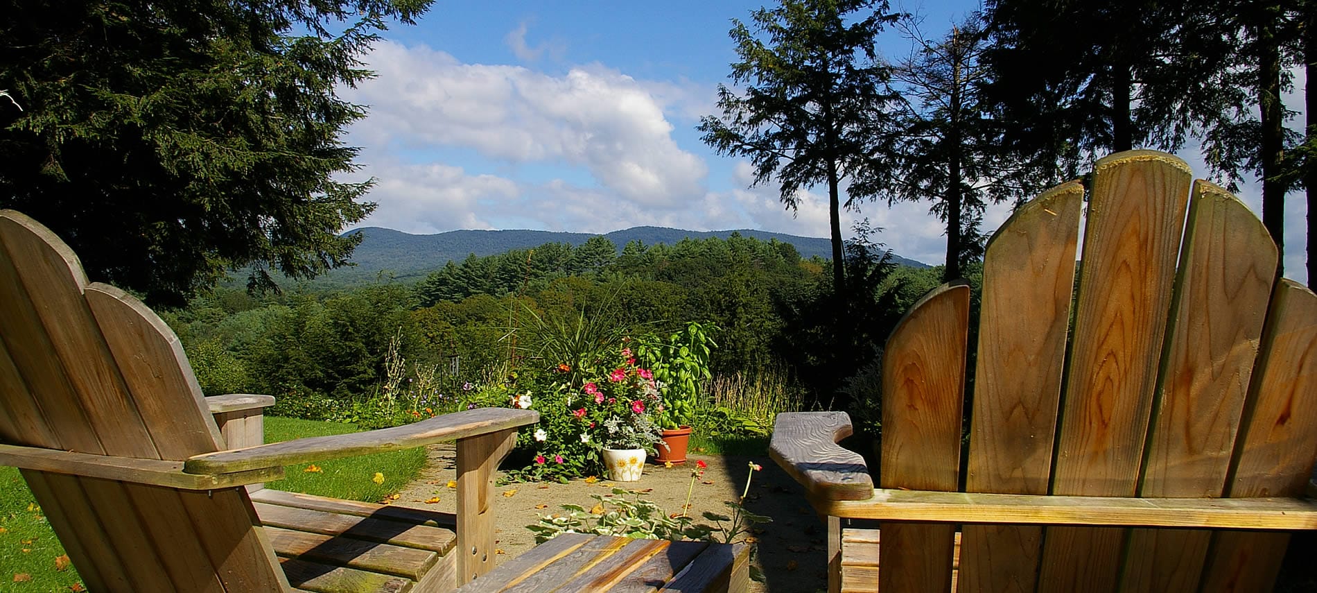 Two wooden Adirondack chairs looking toward the distant hills and trees amidst blue skies