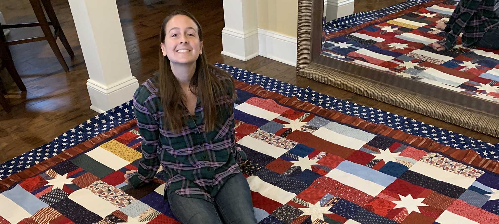 Young woman sitting upon a quilt stretched across a spanse of floor with mirror to show a different angle. Quilt pattern is white 8 point stars on different fields.