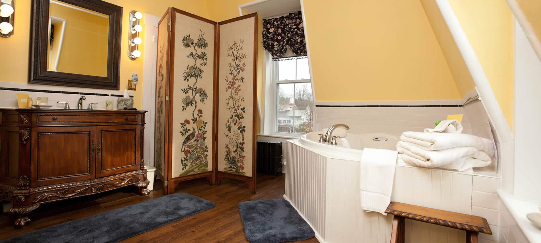 Princess Victoria guest bath with yellow walls, wood floors, antique vanity with sink and white tub