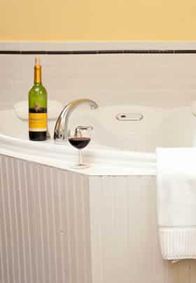 Princess Victoria guest bath tub with white tile and beadboard and wine bottle and glass on edge of tub
